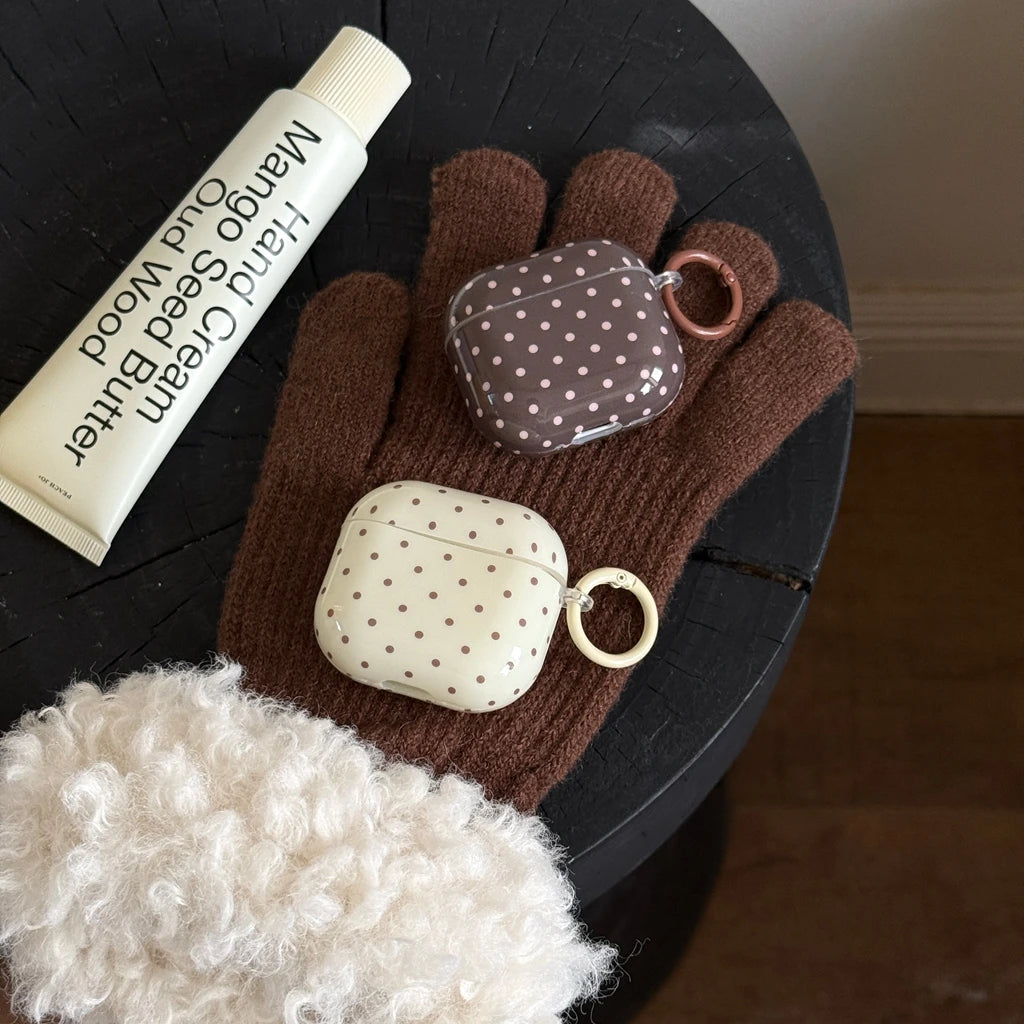 Two glossy, polka-dot AirPods cases in brown and cream, featuring side attachment rings.