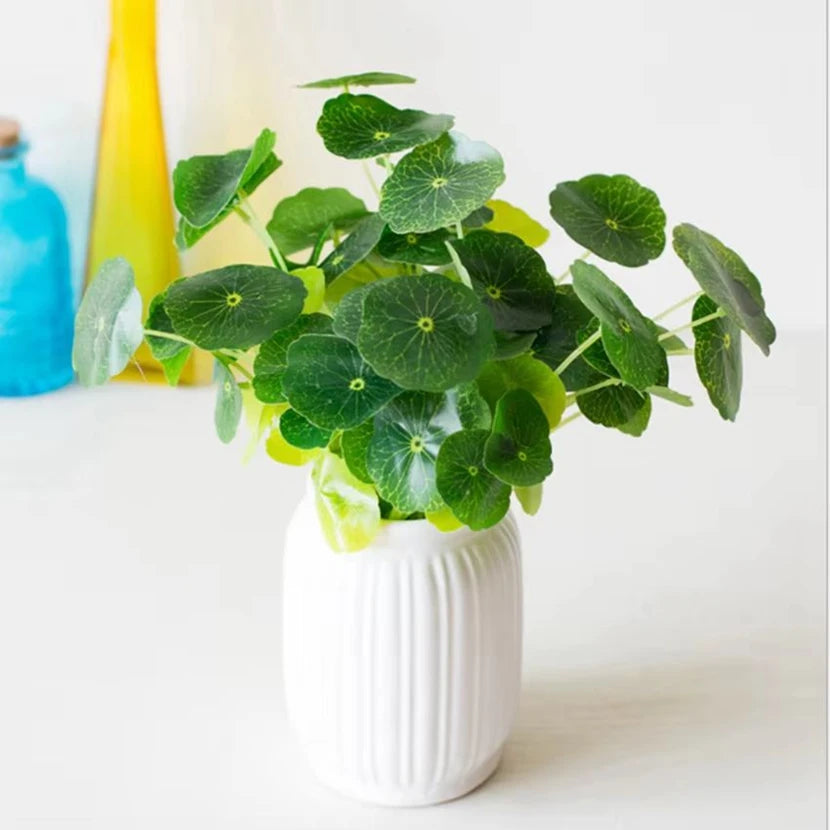 Artificial lotus leaf plant with green, circular leaves in a white ribbed vase against a bright, minimalist background.