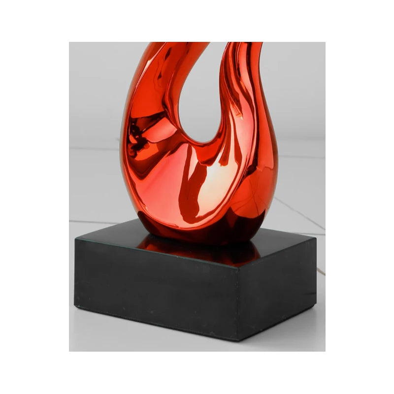 Glossy, red abstract resin ornament with a sculptural, curved design on a rectangular black base.