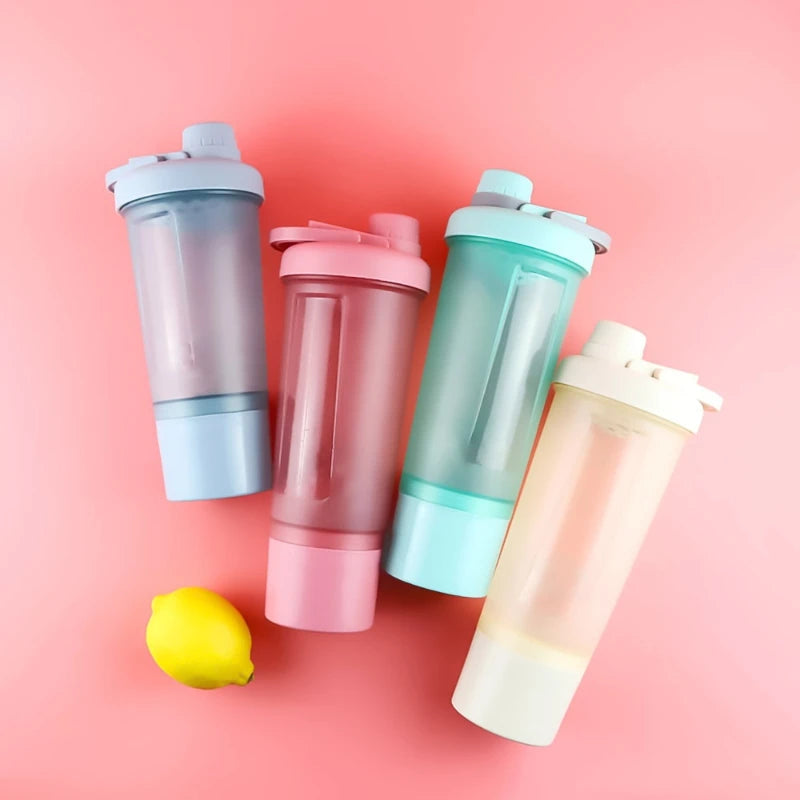 Four pastel-colored plastic protein shaker bottles with flip-top lids, arranged on a pink background with a lemon.