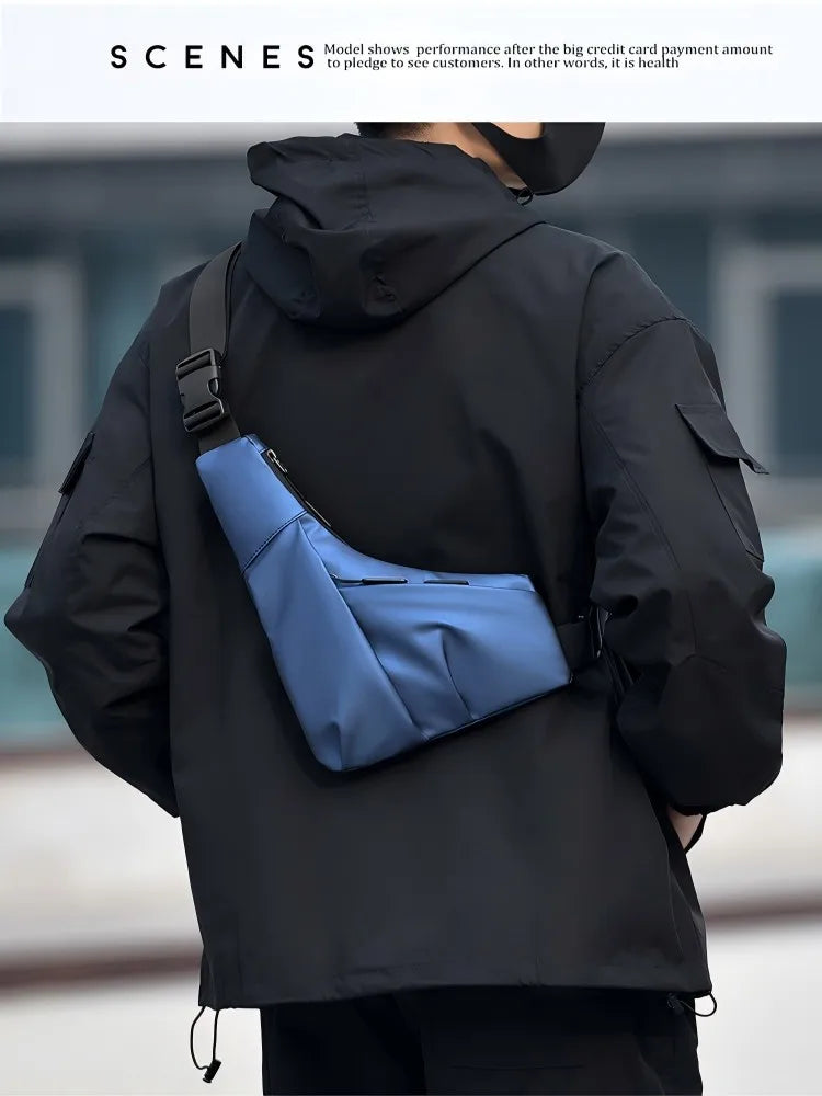 A person wears a slim, blue triangular crossbody bag featuring an adjustable strap and secure zip fastening.
