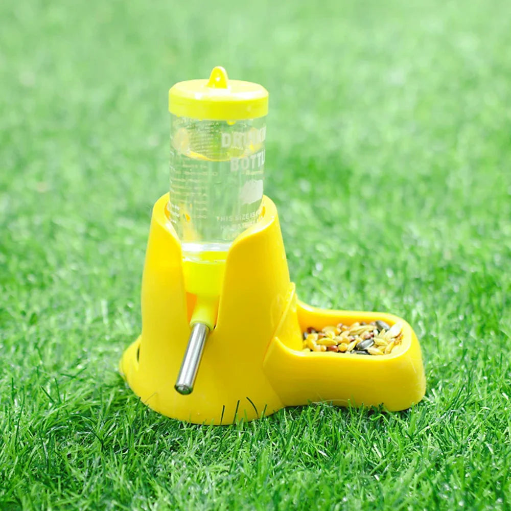 Bright yellow pet feeder with a clear water bottle and metal nozzle, set on green grass.