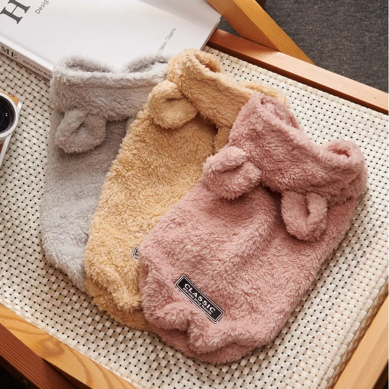 Three soft fleece dog hoodies in grey, beige, and pink with small hoods and a "Classic" label patch.