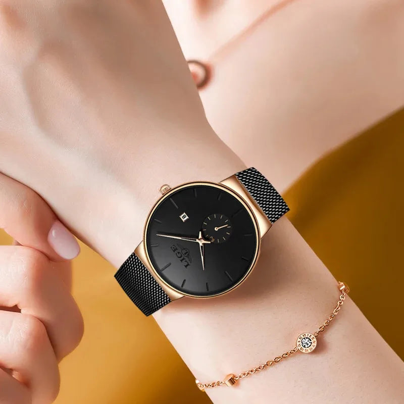 Elegant women's watch with a black face, gold-tone bezel, and slim black stainless steel mesh strap on a wrist.