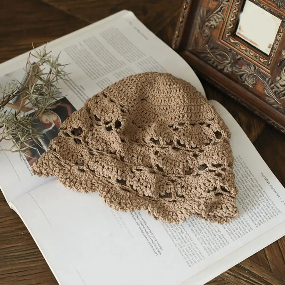 A beige, hollow-patterned crochet lace hat resting on an open magazine.