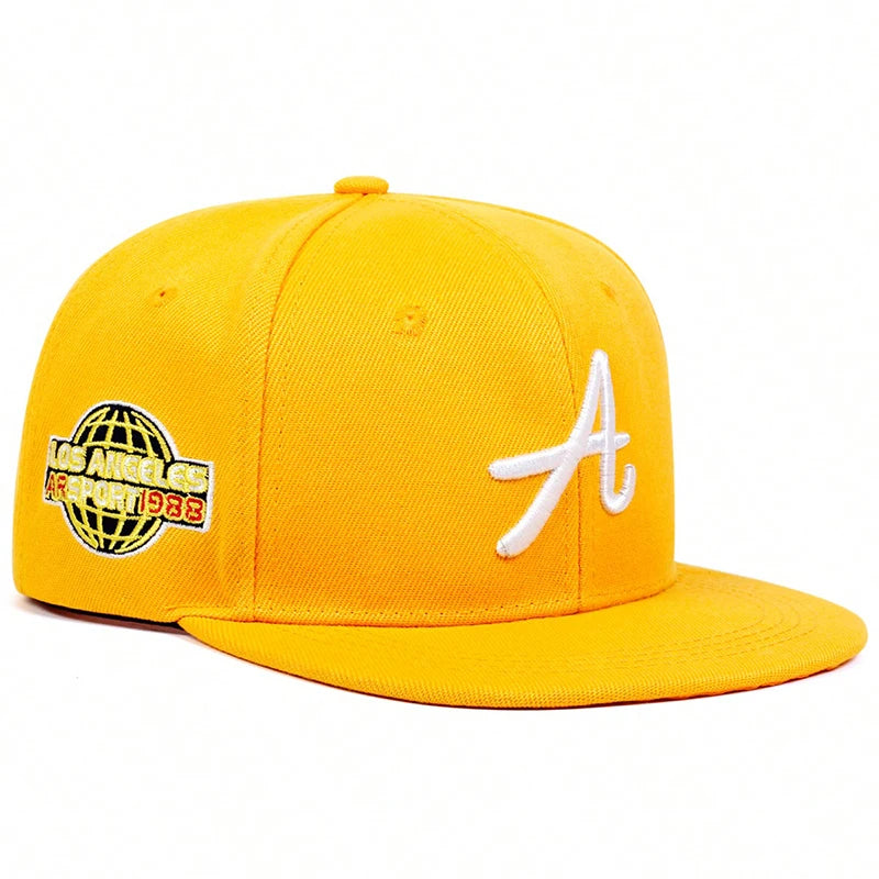 Bright yellow baseball cap with a white cursive 'A' on the front and a globe-themed side patch.