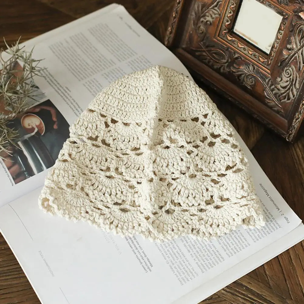 Cream-coloured women's crochet lace hat with a delicate, hollow floral pattern, resting on an open magazine.