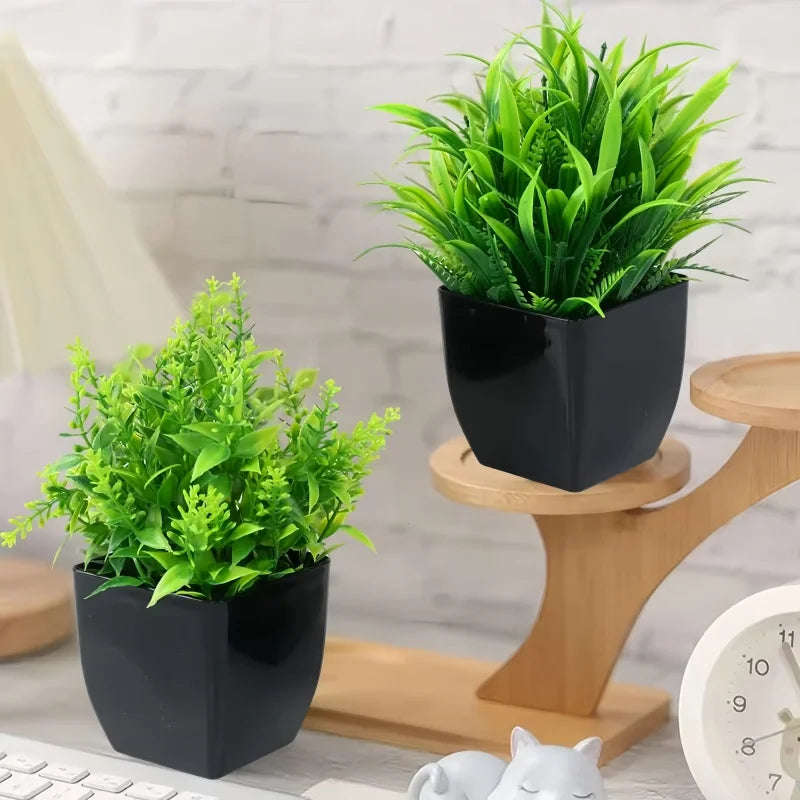 Two artificial green plants in modern, glossy black square pots displayed on a wooden stand with a desk clock.