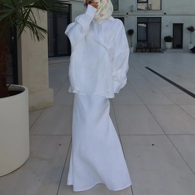 A woman wearing a crisp white oversized button-up shirt and a matching long flowing maxi skirt.
