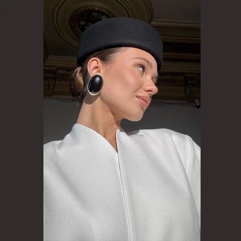 A woman wears an elegant black wool pillbox hat with a structured, flat-top design.