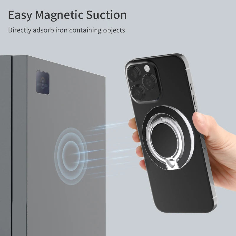 Silver magnetic phone ring holder attached to the back of a black smartphone, shown sticking to a grey metal surface.