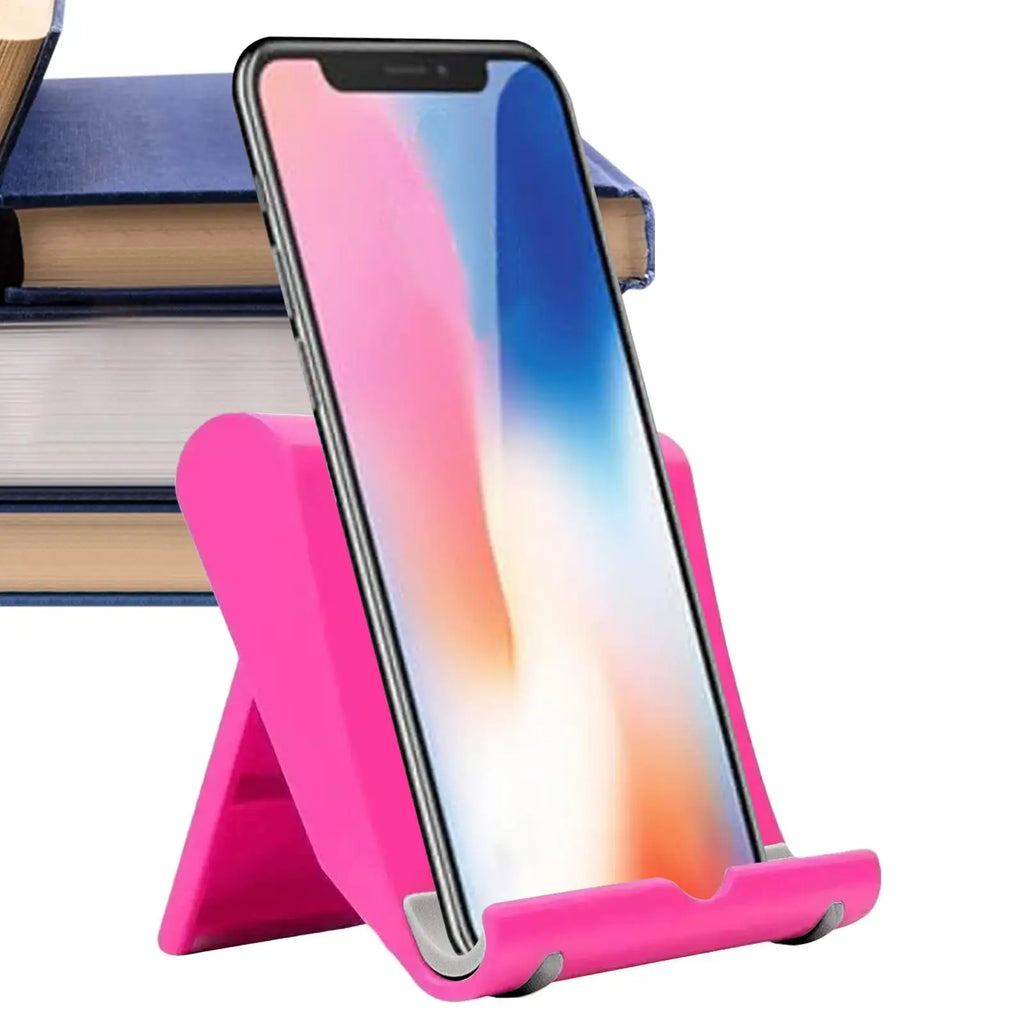 Vibrant pink adjustable smartphone stand holding a phone, sitting on a desk with books in the background.