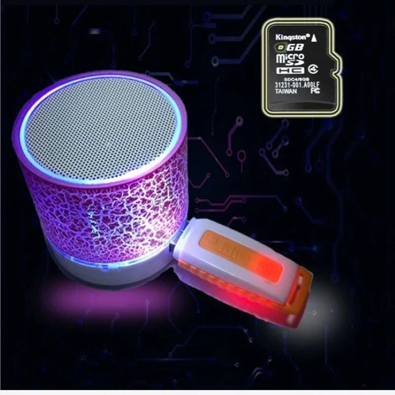 Portable mini wireless speaker with a purple crackle-effect LED light and a white plug-in USB drive on a dark background.