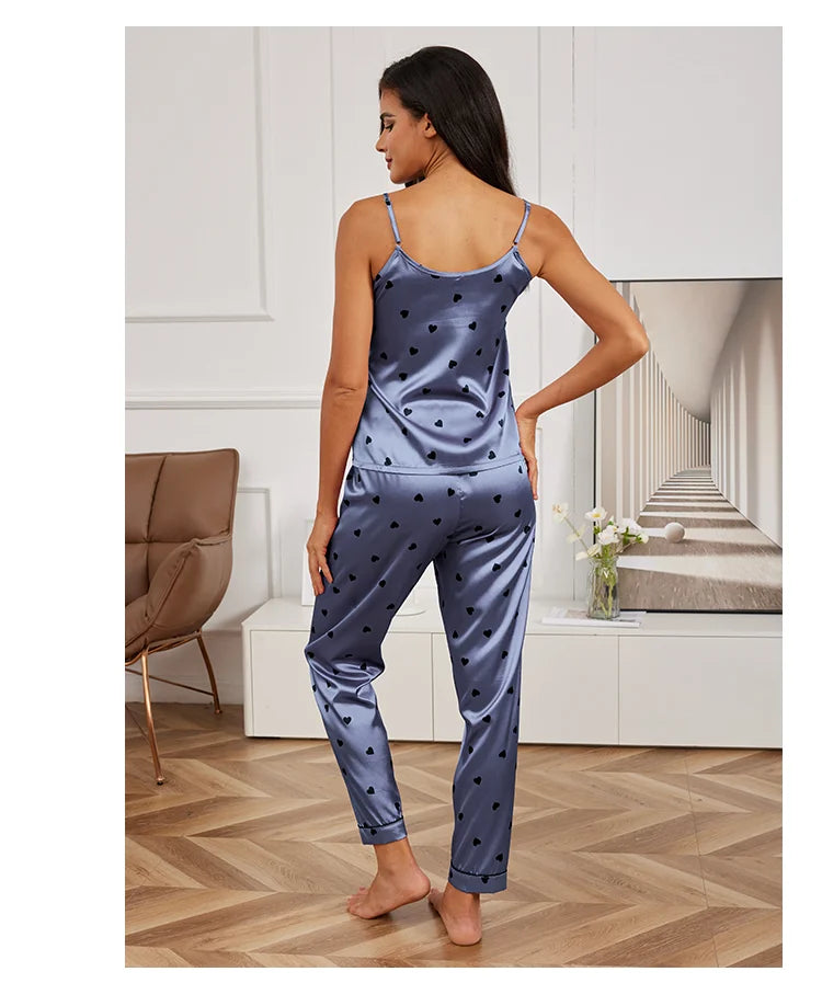 A woman wearing a blue satin pyjama set with a black heart print, featuring a camisole top and matching trousers.