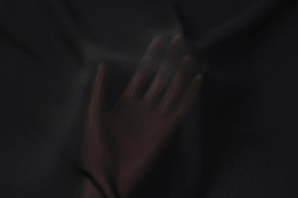 Hand pressed against a piece of soft, sheer black fabric with a subtle drape and smooth texture.