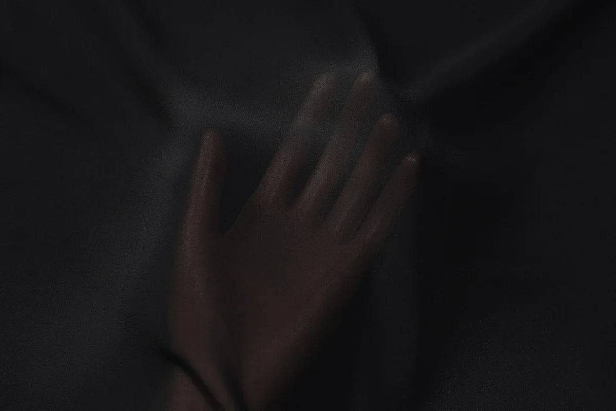 Hand pressed against a piece of soft, sheer black fabric with a subtle drape and smooth texture.
