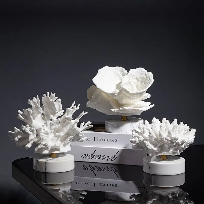 Three white coral sculptures on marble bases, resting on stacked books against a dark background.
