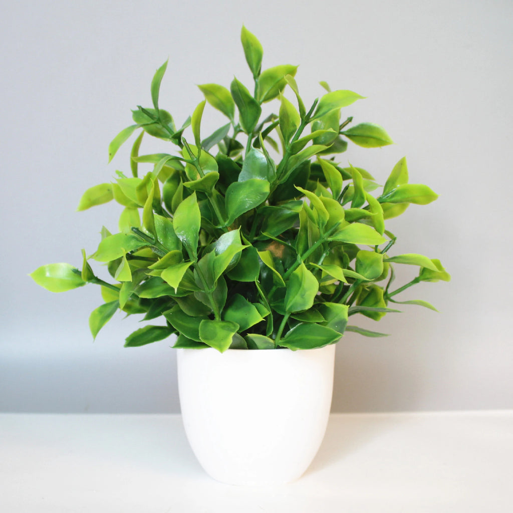 Artificial potted plant with vibrant green leaves in a simple, minimalist white rounded planter against a gray backdrop.