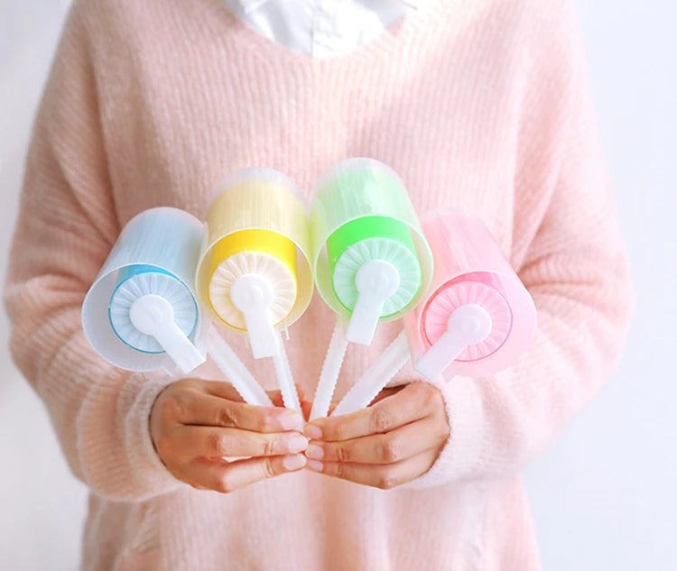 Hands holding four pastel-coloured lint rollers with clear protective covers in blue, yellow, green, and pink.