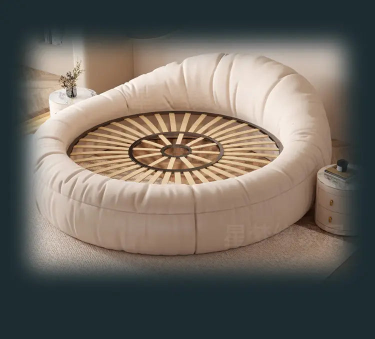 Modern circular cream upholstered bed frame with a minimalist design and exposed wooden slatted base.