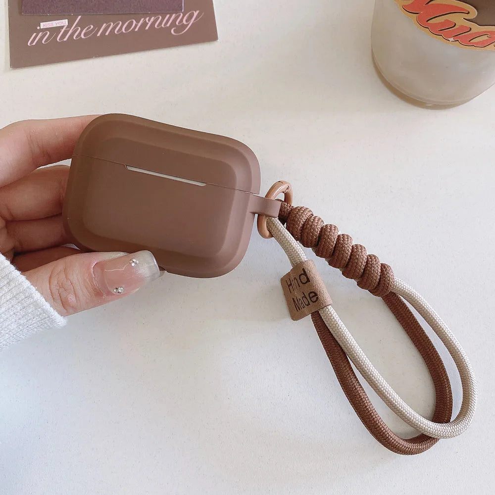 Brown matte silicone AirPods Pro case with a two-tone knotted rope wrist strap and 'Hand Made' tag.