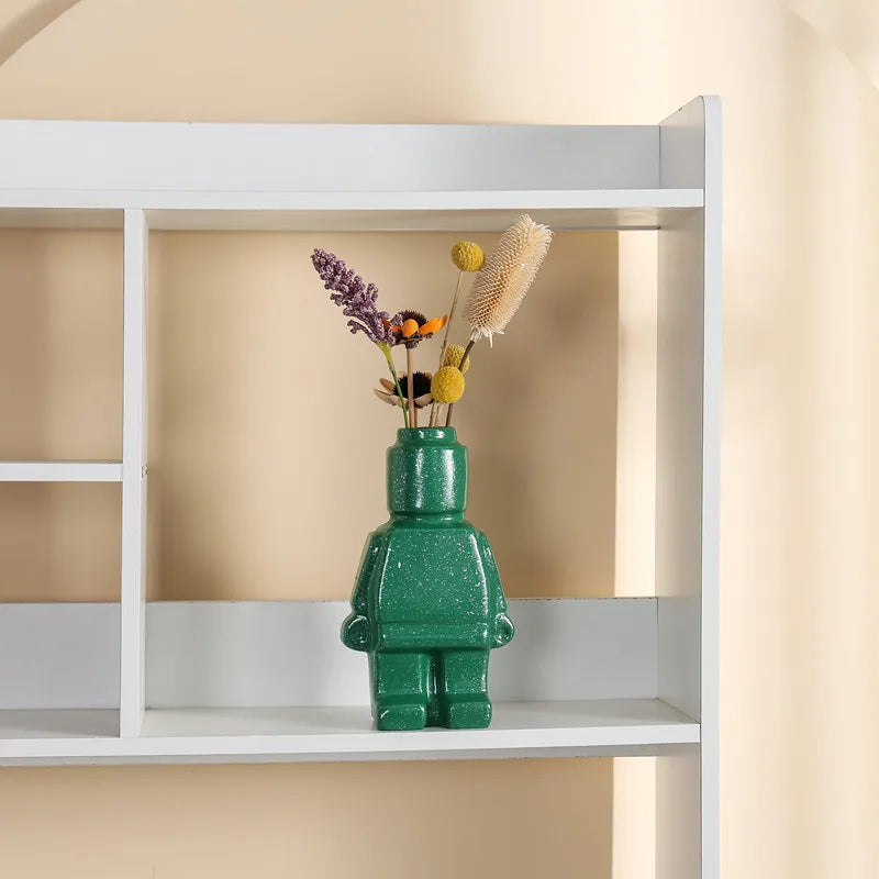 Speckled green ceramic vase in a block-figure shape, holding a small bouquet of dried flowers on a white shelf.