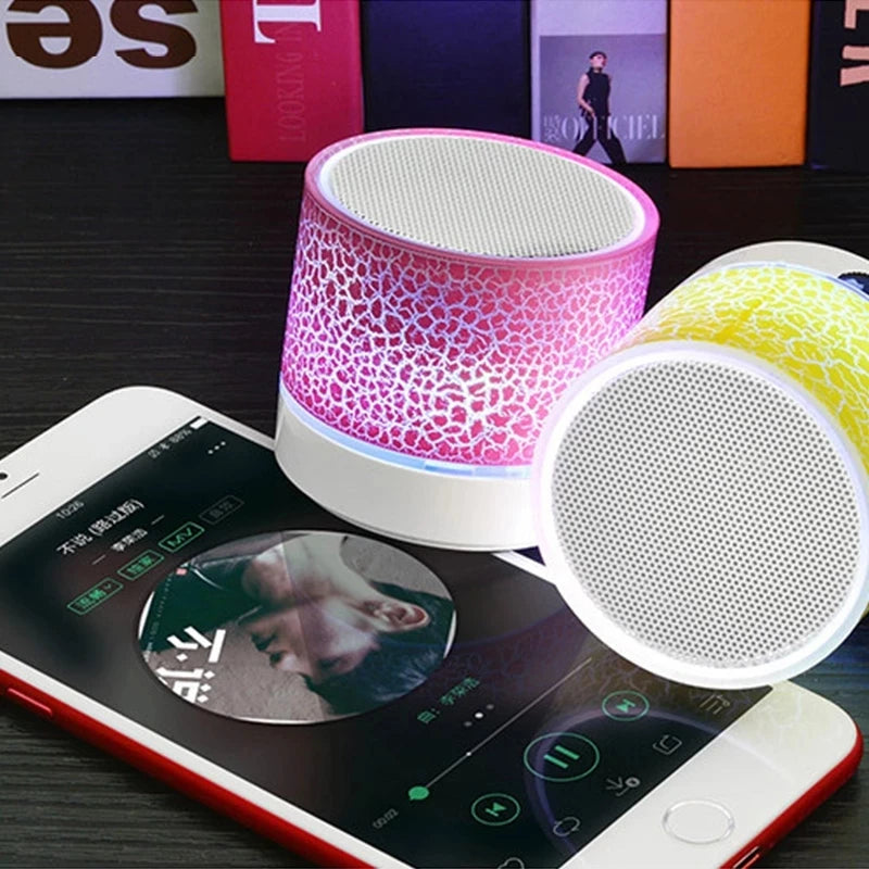 Two portable, circular wireless speakers with a glowing pink and yellow crackle-effect pattern next to a smartphone.