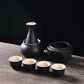 Matte black ceramic sake set with warmer bowl, heating stove, and four matching cups with beige interiors.