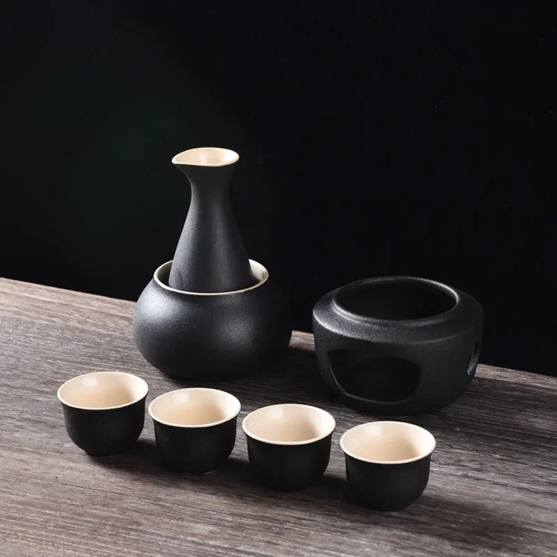 Matte black ceramic sake set with warmer bowl, heating stove, and four matching cups with beige interiors.