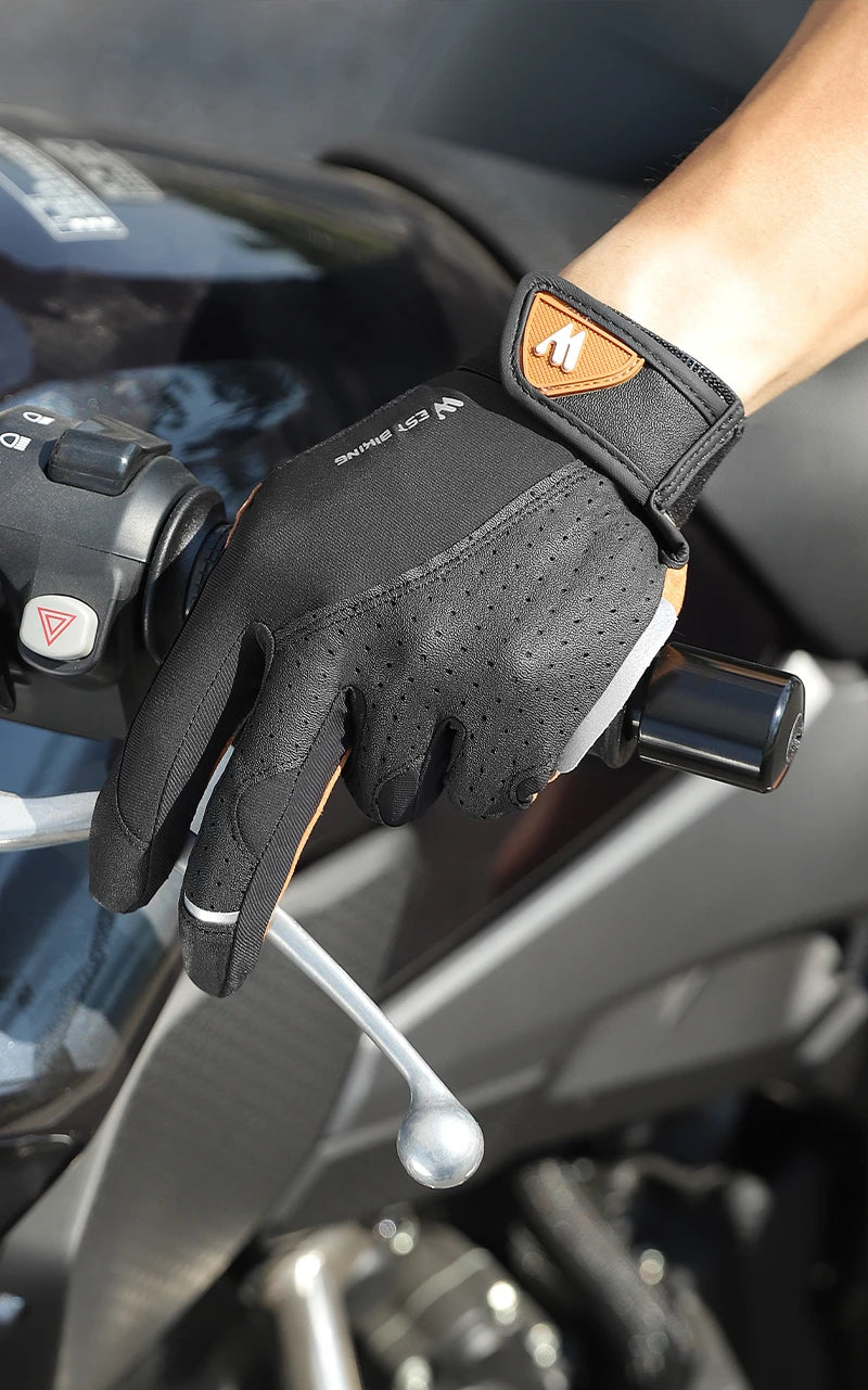 Black motorcycle glove with perforated fabric and tan leather wrist strap, gripping handlebars.
