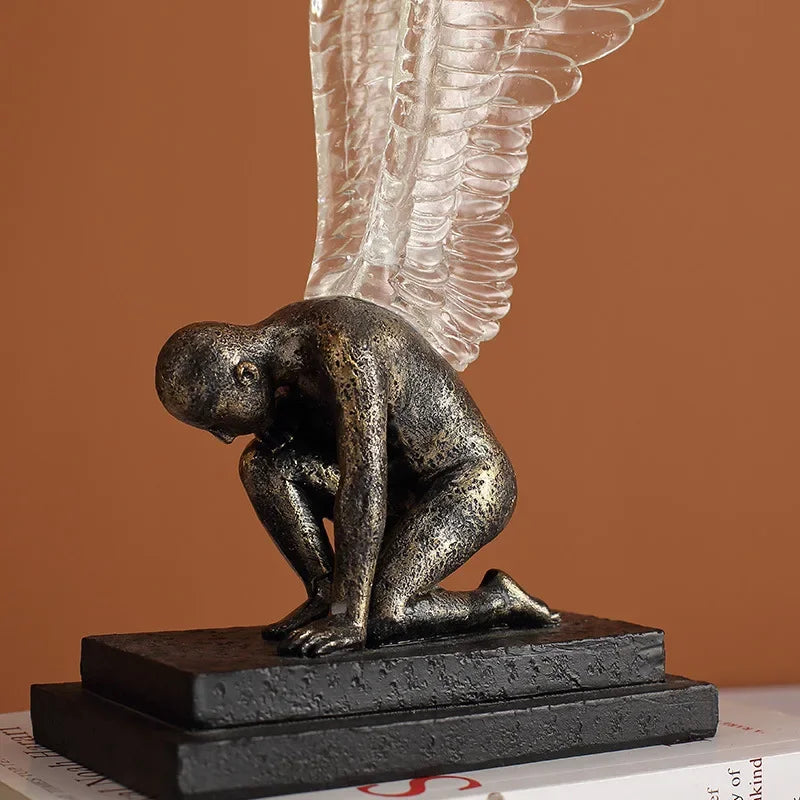 Bronze-effect kneeling angel statue with textured, translucent wings on a rectangular black base.
