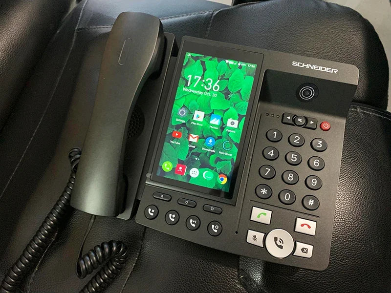 Black VoIP office desk phone with a vertical touchscreen interface, corded handset, and full keypad.
