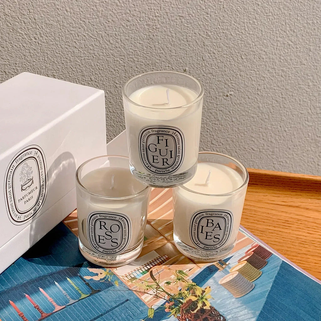 Three small white scented candles in clear glass jars with minimalist oval labels, presented in a white gift box.