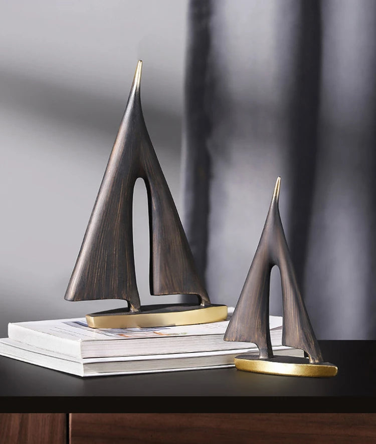 Two abstract resin sailboat ornaments in a dark brushed bronze finish with gold-toned bases, displayed on books.