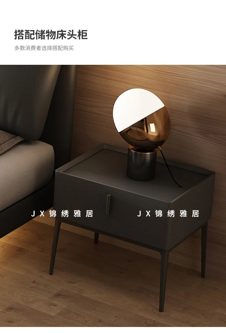 Modern dark grey upholstered bedside table with a sleek drawer and slim black legs, next to a matching bed frame.