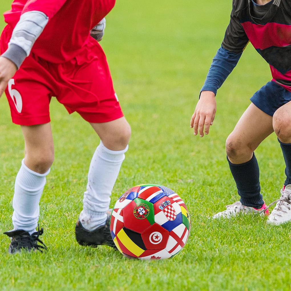 Multicoloured football featuring various international flag designs, placed on a green grass pitch during a game.