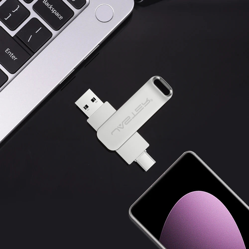 Silver 2-in-1 metal flash drive featuring USB-A and USB-C connectors, placed on a desk near a laptop and smartphone.