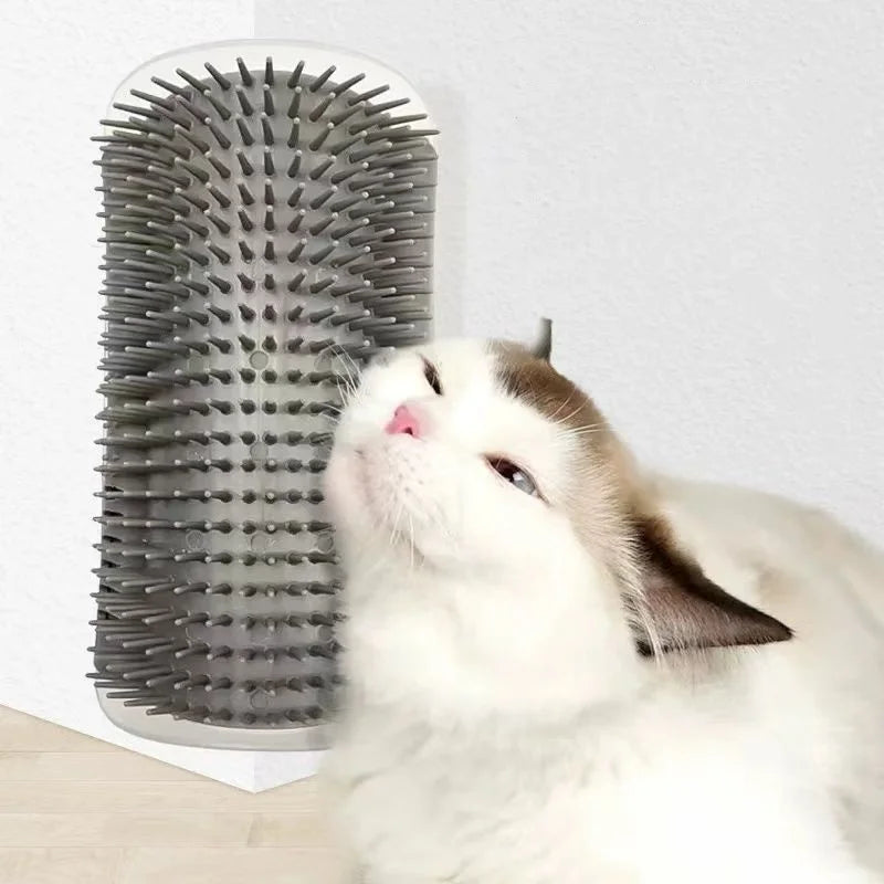 A cat rubs its face against a grey plastic wall-mounted grooming brush with flexible bristles.