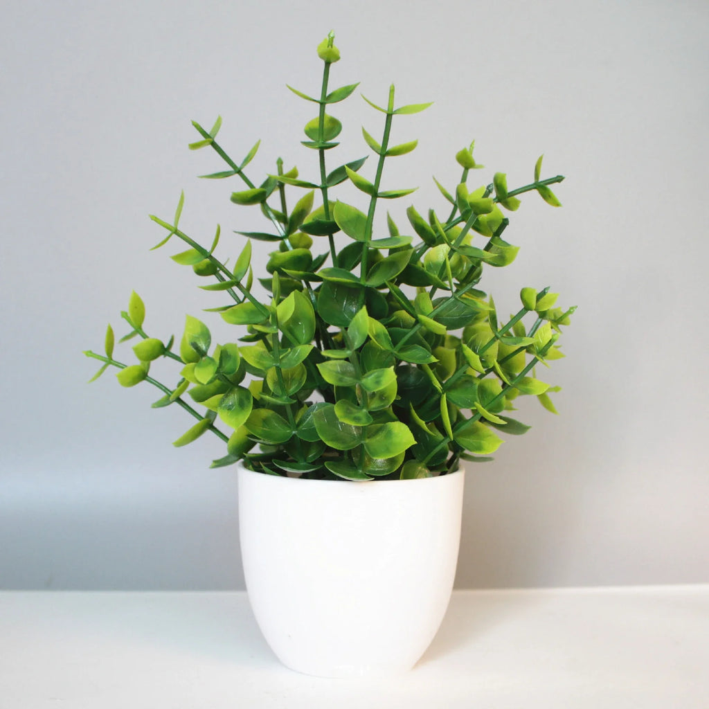 A small, artificial green eucalyptus-style plant in a simple, minimalist white rounded pot against a grey background.