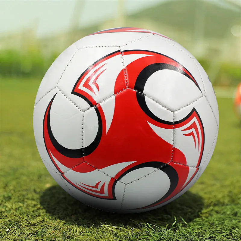 White football with red and black swirl graphic design, featuring classic stitched panels on a grassy field.