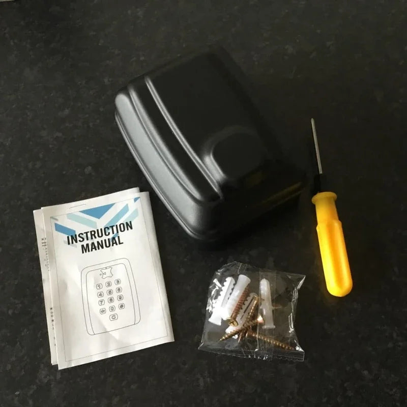 Black plastic wall-mounted key lock box with keypad, instruction manual, screwdriver, and mounting hardware.