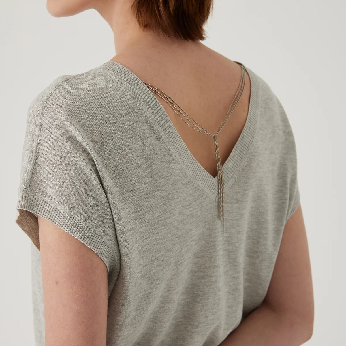 Grey V-neck knit top with delicate, layered gold chain detail across the open back.