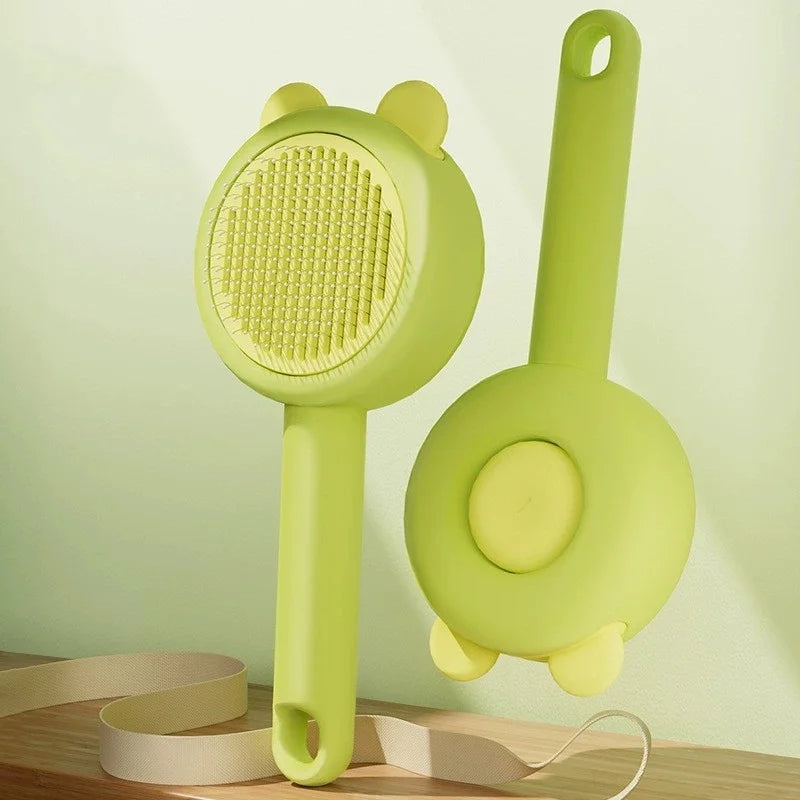 Two light green pet grooming brushes with cute bear-ear detailing, shown from front and back on a wooden surface.
