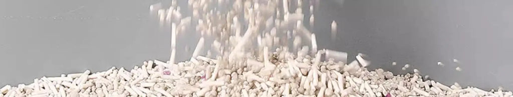 Close-up of pellet-style cat litter being poured onto a smooth, grey waterproof mat.