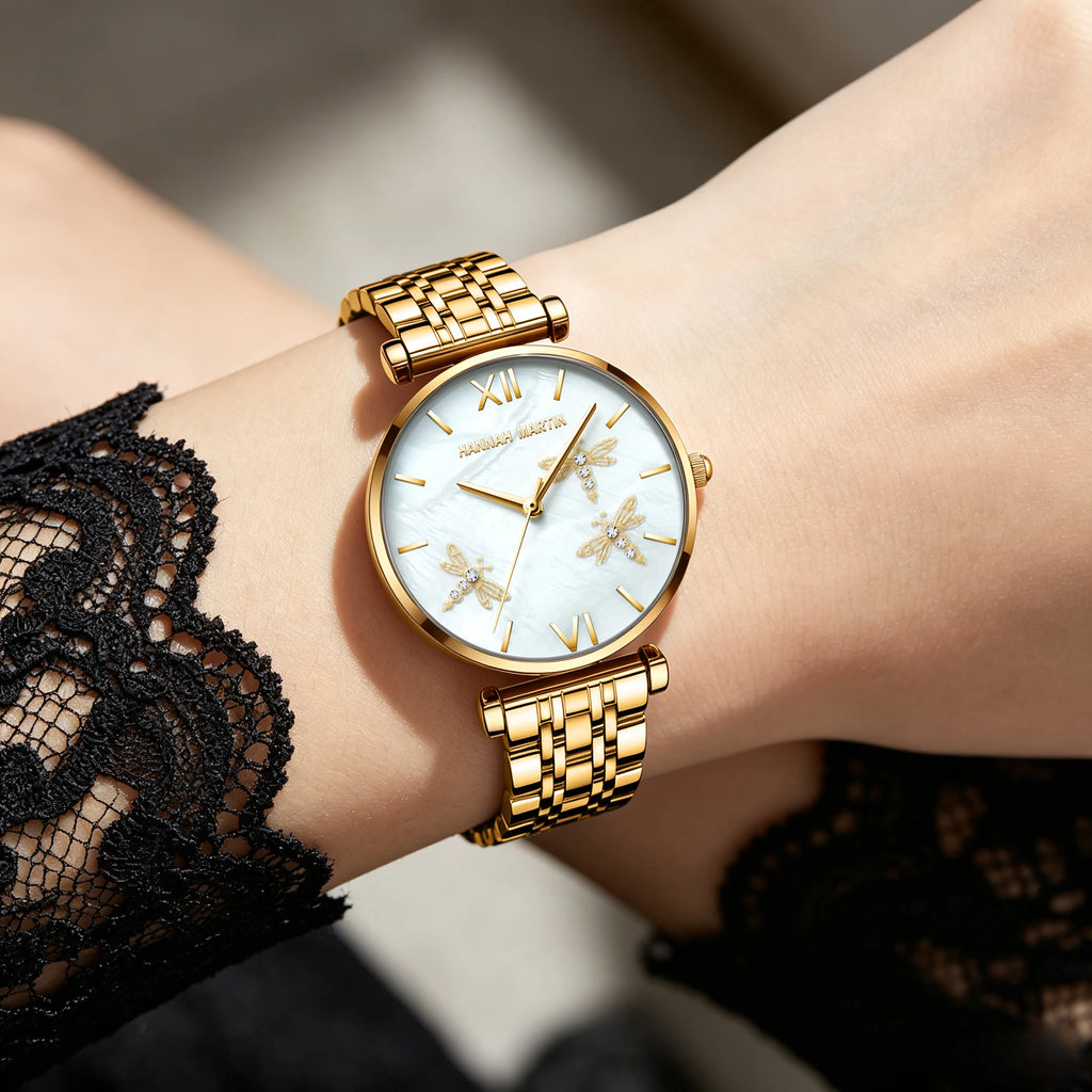 Gold quartz watch with round mother-of-pearl dial, rhinestone-accented dragonfly relief, and linked metal band.