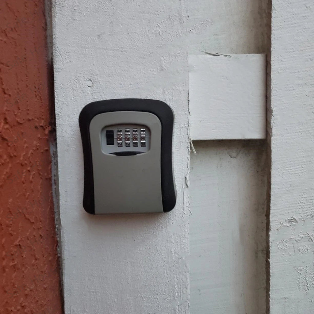Black and grey wall-mounted key lock box with a four-digit combination dial, secured to a white wooden surface.