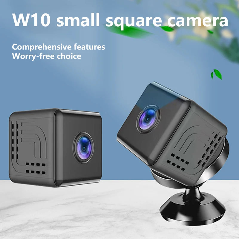 A compact, matte black, square-shaped indoor security camera with a central lens, shown with its magnetic swivel stand.