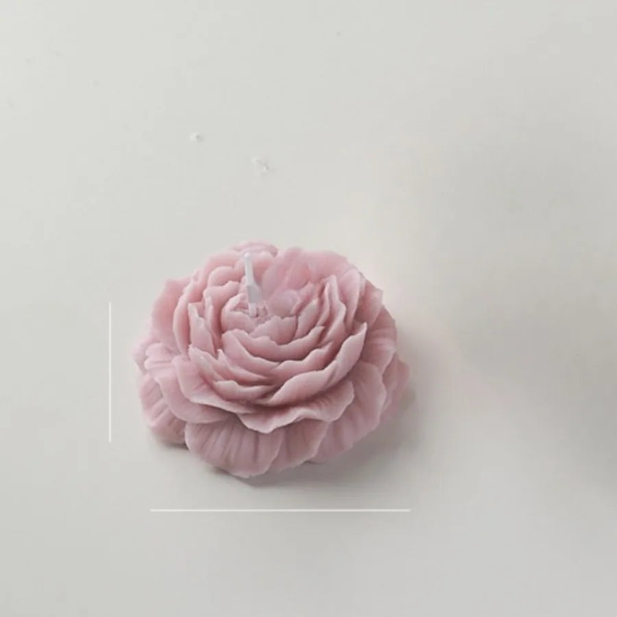 Dusty pink, peony-shaped decorative candle with detailed, layered petals and a central wick on a white background.