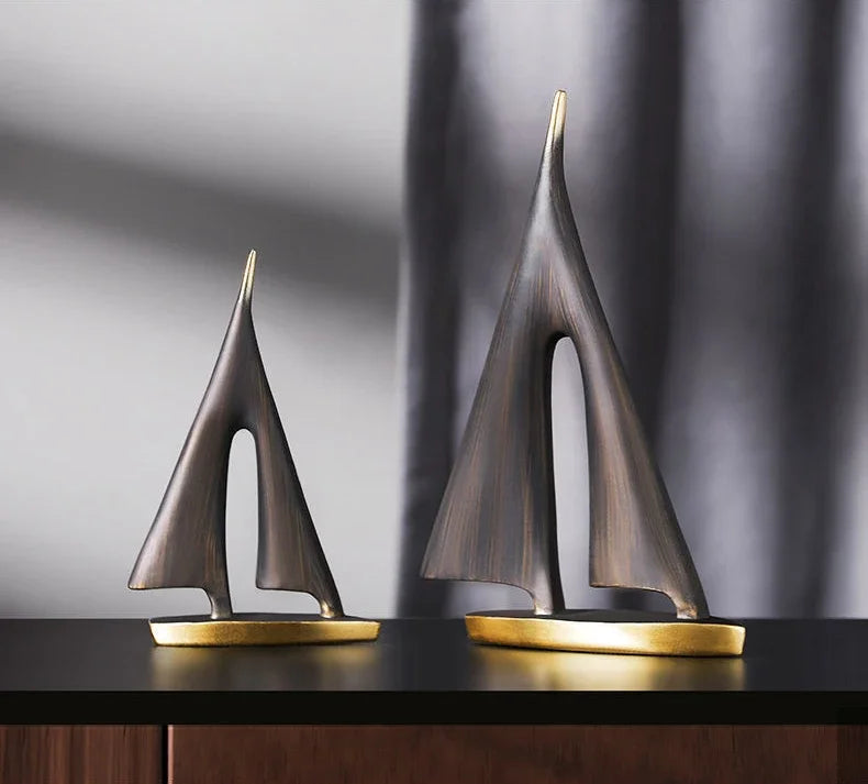 Two abstract resin sailboat ornaments in a dark bronze finish with metallic gold bases on a dark surface.