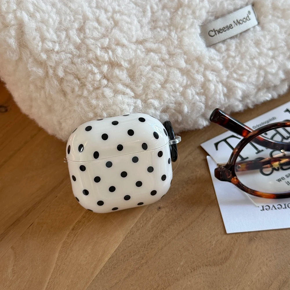 Glossy white AirPods Pro case with black polka dot print, featuring a side loop for attachment.